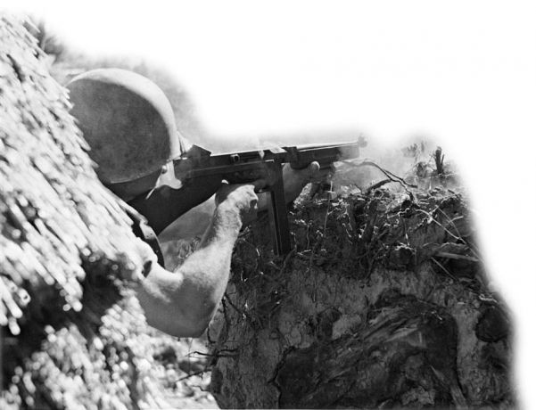 An American soldier fires his Thompson submachine gun against a Japanese position on Cibik Ridge, Bougainville
