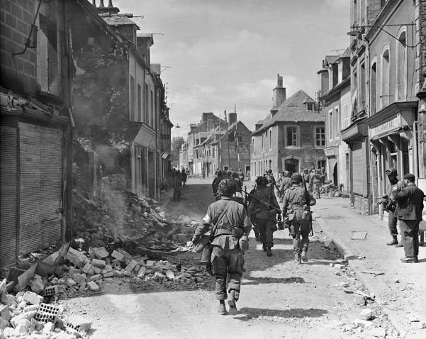 American troops march through bomb-damaged Carentan, the first French city to fall to the invaders after D-Day